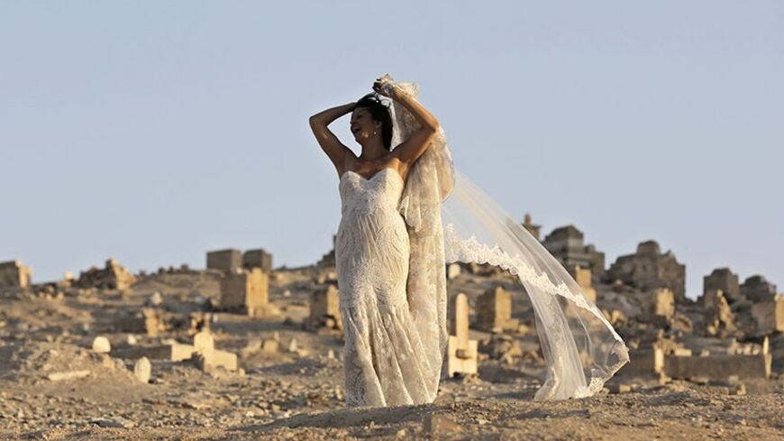 An Israeli bride poses for her wedding photographer (not pictured) as graves are seen in the background at Nabi Musa Muslim Cemetery in the Judean desert near the West Bank city of Jericho November 28, 2013. REUTERS/Ammar Awad (WEST BANK - Tags: SOCIETY) - RTX15WJZ