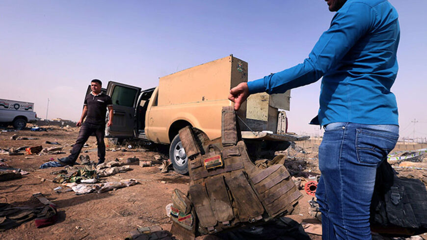 A man displays Iraqi army body armour in front of an Iraqi army vehicle and other items of military kit, at the Kukjali Iraqi Army checkpoint, some 10km of east of the northern city of Mosul, on June 11, 2014, the day after Sunni militants iincluding fighters from the Islamic State of Iraq and the Levant (ISIL) overran the city.  Half a million people were estimated to have fled Iraq's second largest city, as Islamist militants tightened their grip after overrunning it and a swathe of other territory, patro