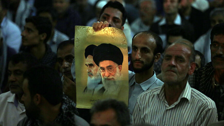An Iranian man holds a photo showing Iran's supreme leader Ayatollah Ali Khamenei, and Iran's late Ayatollah Ruhollah Khomeini, while listening to Iran's President Hassan Rouhani delivering a speech on the eve of the 25th anniversary of the death of Islamic revolutionary leader Khomeini, at Khomeini's mausoleum in a suburb of Tehran on June 3, 2014. AFP PHOTO / ATTA KENARE        (Photo credit should read ATTA KENARE/AFP/Getty Images)