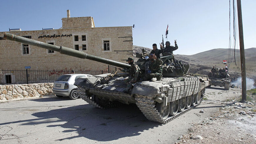 Soldiers loyal to Syria's President Bashar al-Assad gesture from their tank, as they pass Mar Bacchus Sarkis monastery, in Maloula village, northeast of Damascus, after taking control of the village from rebel fighters April 14, 2014. REUTERS/Khaled al-Hariri (SYRIA - Tags: MILITARY POLITICS CONFLICT CIVIL UNREST TPX IMAGES OF THE DAY) - RTR3L92W