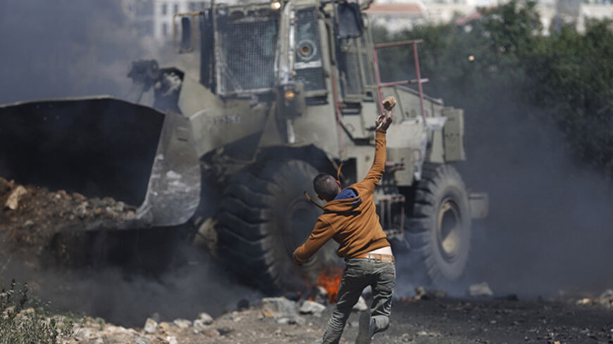 A Palestinian protester throws a stone towards an Israeli military bulldozer during a protest against the Jewish settlement of Qadomem, near the West Bank City of Nablus May 2, 2014. REUTERS/Mohamad Torokman (WEST BANK - Tags: POLITICS CIVIL UNREST) - RTR3NJYG