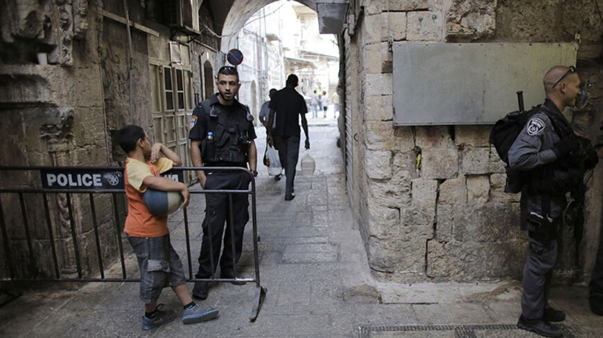 A Palestinian boy stands next to an Israeli policeman at a police barrier in Jerusalem's Old City June 2, 2014. REUTERS/Ammar Awad (JERUSALEM - Tags: POLITICS SOCIETY) - RTR3RW4G