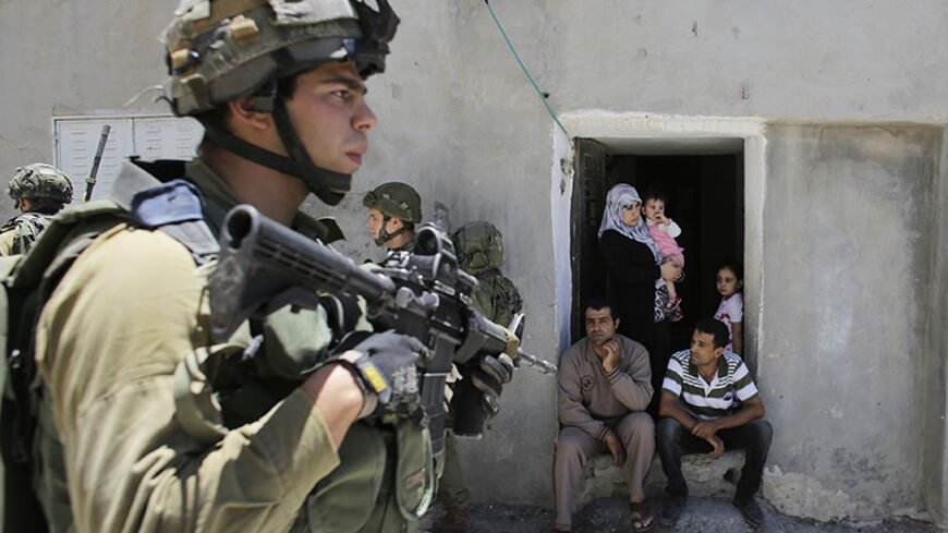 Palestinians sit outside their house as Israeli soldiers patrol near the West Bank City of Hebron June 15, 2014. Israel said on Sunday Hamas militants had abducted three Israeli teenagers in the occupied West Bank, warning of "serious consequences" as it pressed on with a search and detained dozens of Palestinians.   REUTERS/Ammar Awad (WEST BANK - Tags: POLITICS CIVIL UNREST MILITARY) - RTR3TVBR