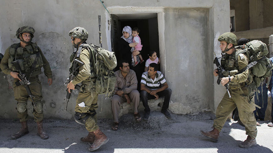Palestinians sit outside their house as Israeli soldiers patrol near the West Bank City of Hebron June 15, 2014. Israel said on Sunday Hamas militants had abducted three Israeli teenagers in the occupied West Bank, warning of "serious consequences" as it pressed on with a search and detained dozens of Palestinians. REUTERS/Ammar Awad (WEST BANK - Tags: POLITICS CIVIL UNREST MILITARY) - RTR3TVDN