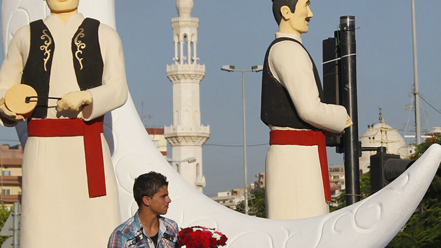 A vendor sits near statues of Musaharati, or dawn awakeners, erected as part of decorations ahead of the holy fasting month of Ramadan at the port city of Sidon, southern Lebanon June 25, 2014.  REUTERS/Ali Hashisho (LEBANON - Tags: RELIGION) - RTR3VQ1L