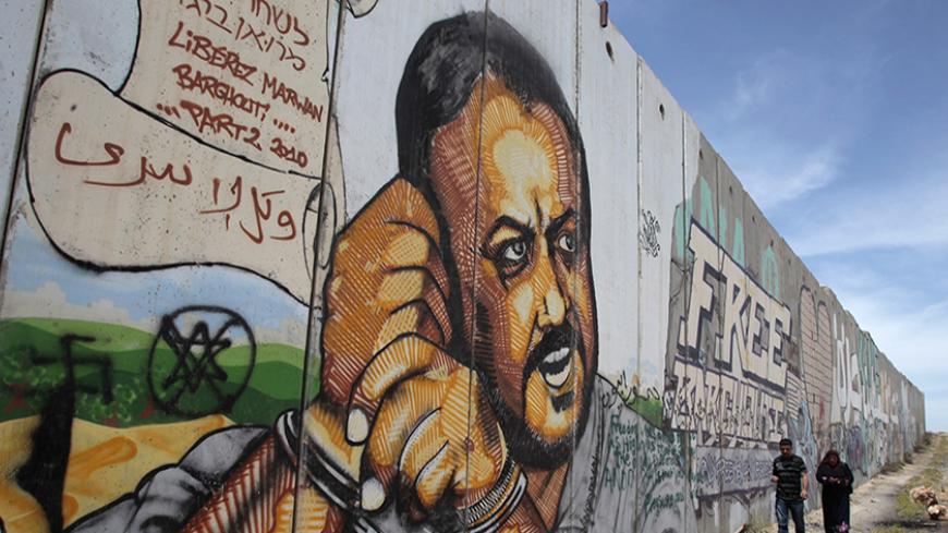 Palestinians walk past graffiti depicting jailed Fatah leader Marwan Barghouti on a section of the controversial Israeli barrier near the Qalandiya checkpoint outside the West Bank city of Ramallah May 25, 2011. Palestinians and Israelis alike saw little prospect of a fresh start to Middle East peace talks on Wednesday after Israeli Prime Minister Benjamin Netanyahu's keynote speech to Congress. REUTERS/Baz Ratner (WEST BANK - Tags: POLITICS) - RTR2MVS6