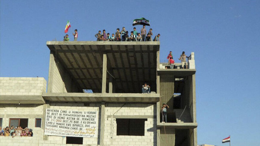 Youths wave Kurdish and Syrian opposition flags from the top of a building during a protest against Syria's President Bashar al-Assad at Kobani near Aleppo July 3, 2012. Picture taken July 3, 2012. REUTERS/Shaam News Network/Handout (SYRIA - Tags: POLITICS CIVIL UNREST) FOR EDITORIAL USE ONLY. NOT FOR SALE FOR MARKETING OR ADVERTISING CAMPAIGNS. THIS IMAGE HAS BEEN SUPPLIED BY A THIRD PARTY. IT IS DISTRIBUTED, EXACTLY AS RECEIVED BY REUTERS, AS A SERVICE TO CLIENTS - RTR34KQ3