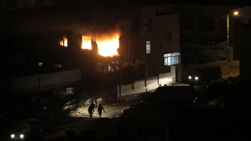 Israeli soldiers walk as flames are seen at the family home of an alleged abductor after a blast on the top floor in the West Bank City of Hebron July 1, 2014. The bodies of three missing Israeli teenagers were found in the occupied West Bank, and Israel vowed to punish Hamas, the Palestinian group it accuses of abducting and killing them. Troops set off explosions in the family homes of the alleged abductors, blowing open a doorway in one, an army spokeswoman said, while television footage showed the other