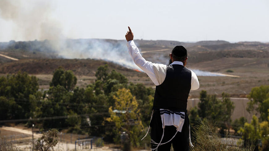 An ultra-Orthodox Jew speaking on a mobile phone gestures in front of a fire that broke out after a rocket landed near the southern town of Sderot July 9, 2014. Israeli air strikes shook Gaza every few minutes on Wednesday, and militants kept up rocket fire at Israel's heartland in intensifying warfare that Palestinian officials said has killed at least 37 people in the Hamas-dominated enclave. REUTERS/Ronen Zvulun (ISRAEL - Tags: POLITICS MILITARY CIVIL UNREST RELIGION) - RTR3XTBG