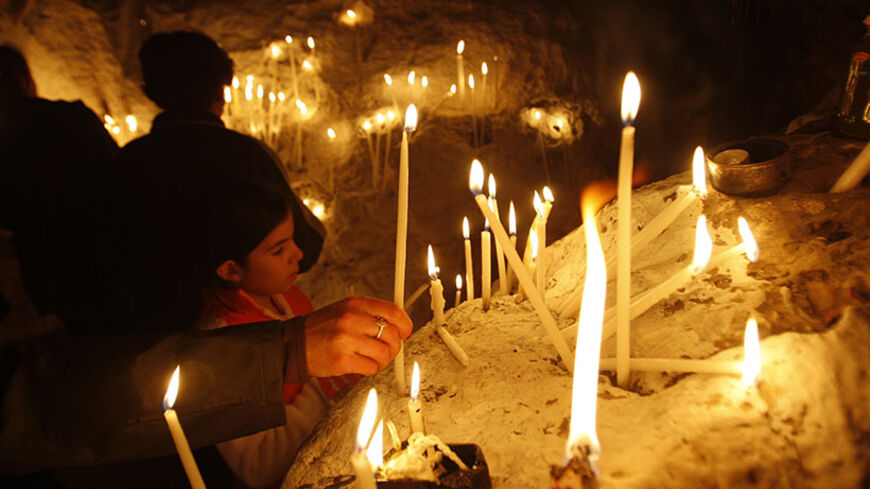 A Palestinian Roman Orthodox Christian girl looks at candles as they are lit inside an old cave which residents say is used as a church, in the West Bank village of Aboud near Ramallah, ahead of Christmas December 16, 2010. REUTERS/Mohamad Torokman (WEST BANK - Tags: RELIGION) - RTXVSYL