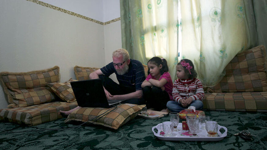 Omar Odeh, a Palestinian refugee from from the Yarmuk refugee camp in Damascus who fled Syria some two months ago, sits with his daughters as he looks at his laptop in the livingroom of their rented apartment in the Jabalia refugee camp in the Gaza Strip on  April 16, 2013.  Odeh who fled Syria last year, was followed by his Palestinian mother, Syrian wife Basma and their children in February transiting through Egypt to reach the Gaza Strip. Finding no work, they are living off donated aid and help from fam