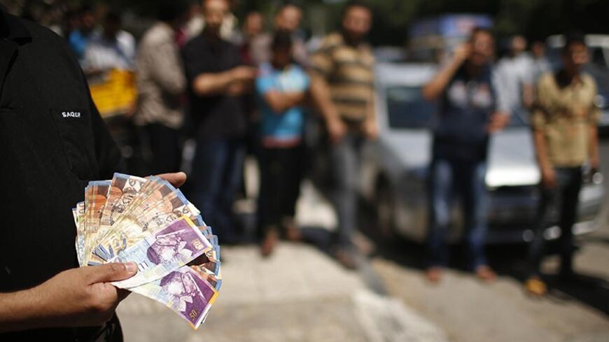 A Palestinian employee paid by the Palestinian Authority shows money to the camera after withdrawing cash from an ATM machine outside a bank, in Gaza City June 11, 2014. Gaza's public sector union suspended protests on Wednesday that had paralysed the local economy and threatened the deal on a Palestinian unity government but said it would resume its action if its members were not promptly paid. The pay dispute involving some 40,000 public servants erupted last week shortly after Hamas, which has ruled Gaza