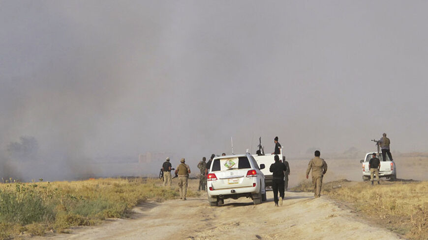 Shi'ite volunteers from the Mehdi Army loyal to radical cleric Muqtada al-Sadr, patrol in vehicles, as smoke rises from clashes with Islamic State fighters, on the outskirts of Tikrit, July 20, 2014. Iraqi troops and Shi'ite militants patrolled areas of Tikrit as they launched an assault to retake the city currently held by Islamic State fighters.  REUTERS/Stringer (IRAQ - Tags - Tags: CIVIL UNREST POLITICS MILITARY) - RTR3ZG0I