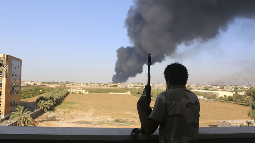 A fighter from Zintan brigade watches as smoke rises after rockets fired by one of Libya's militias struck and ignited a fuel tank in Tripoli August 2, 2014. On Saturday, sporadic shelling resumed in the capital after two days of relative calm. Plumes of black smoke rose over the south of Tripoli from a burning fuel tank at the airport's fuel depot. REUTERS/Hani Amara (LIBYA - Tags: POLITICS CIVIL UNREST) - RTR411E4