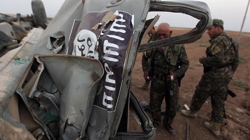 Peshmerga fighters inspect the remains of a car, bearing an image of the trademark jihadist flag, which belonged to Islamic State (IS) militants after it was targeted by an American air strike in the village of Baqufa, north of Mosul, on August 18,2014. Kurdish peshmerga fighters backed by federal forces and US warplanes pressed a counter-offensive Monday against jihadists after retaking Iraq's largest dam, as the United States and Britain stepped up their military involvement. AFP PHOTO/AHMAD AL-RUBAYE    