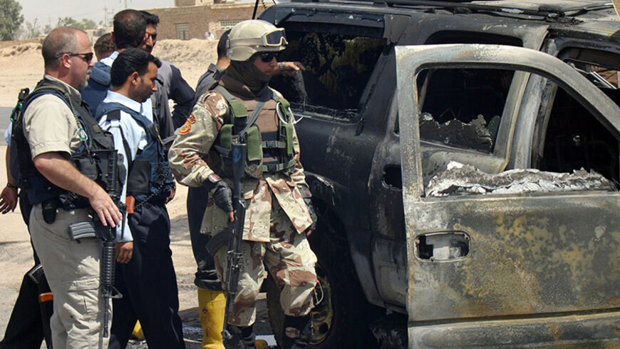 A private security contractor (L) and soldiers look at a destroyed vehicle after an attack near the Iraqi city of Najaf May 18, 2006. Witnesses said a roadside bomb exploded near a convoy of vehicles commonly used by private security firms, killing one Iraqi policeman.   REUTERS/Ali Abu Shish - RTR1DHVM