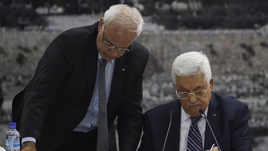 Palestinian chief negotiator Saeb Erekat (L) helps Palestinian President Mahmoud Abbas as he signs international conventions during a meeting with Palestinian leadership in the West Bank City of Ramallah April 1, 2014. Abbas signed more than a dozen international conventions on Tuesday citing anger at Israel's delay of a prisoner release, in a move jeopardised U.S. efforts to salvage fragile peace talks. REUTERS/Mohamad Torokman (WEST BANK - Tags: POLITICS) - RTR3JIOF