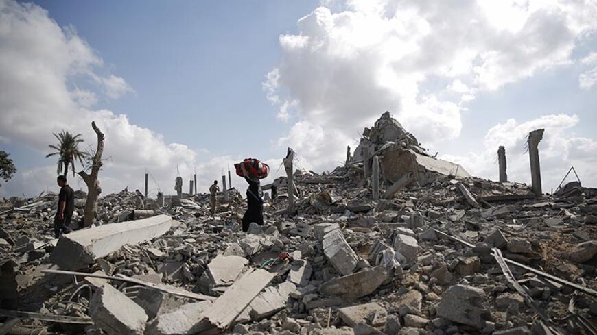 A Palestinian woman carries belongings as she walks over the rubble of buildings destroyed by what police said were Israeli air strikes and shelling in Khuzaa, east of Khan Younis, in the southern Gaza Strip August 3, 2014. An Israeli air strike killed at least 10 people and wounded about 30 others on Sunday in a U.N.-run school in the southern Gaza Strip, a Palestinian official said, as dozens died in Israeli shelling of the enclave and Hamas fired rockets at Israel. The Israeli military said it was lookin