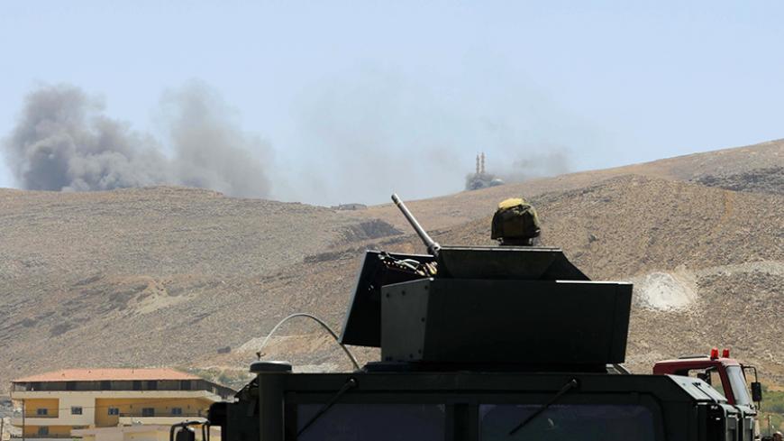 A Lebanese army soldier sits atop an army vehicle at the entrance of the Sunni Muslim border town of Arsal, in eastern Bekaa Valley, as smoke rises during clashes between Lebanese army soldiers and Islamist militants August 4, 2014. The Lebanese army advanced into a border town that was attacked by Islamists in an incursion from Syria at the weekend, finding the bodies of 50 militants, a Lebanese security official said.     REUTERS/Hassan Abdallah    (LEBANON - Tags: POLITICS CIVIL UNREST MILITARY TPX IMAGE