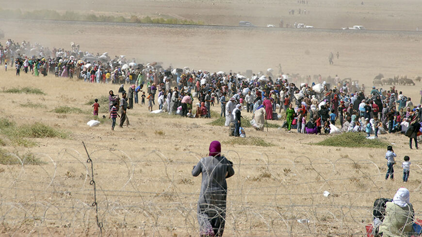 Syrian Kurds wait behind the border fence to cross into Turkey near the southeastern town of Suruc in Sanliurfa province, September 19, 2014. Several thousand Syrian Kurds began crossing into Turkey on Friday fleeing Islamic State fighters who advanced into their villages, prompting warnings of massacres from Kurdish leaders. Islamic State (IS) fighters have seized villages in northern Syria over the past two days and are besieging the mainly Kurdish town of Ayn al-Arab, known as Kobani in Kurdish, on the T