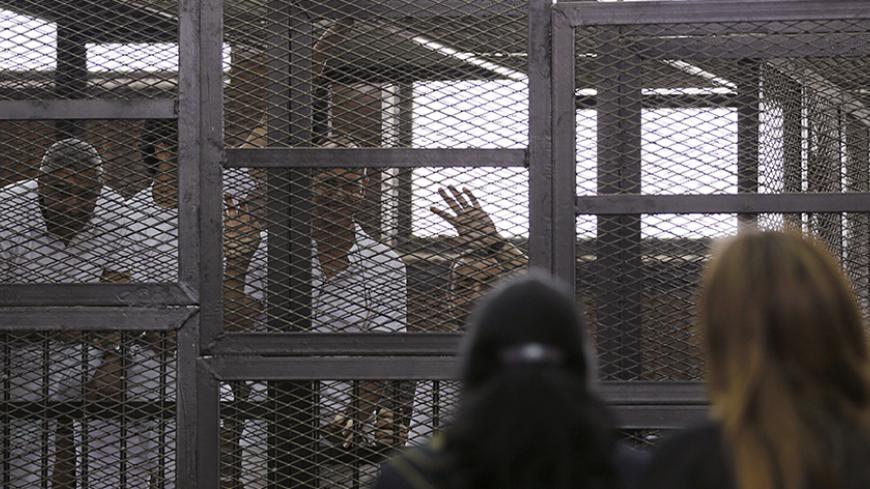 Al Jazeera journalists (L-R) Mohammed Fahmy, Peter Greste and Baher Mohamed wave to a friend and Fahmy's fiancee as they stand behind bars in a court in Cairo June 1, 2014. The trial of the three Al Jazeera journalists accused of aiding of a "terrorist organisation" has been postponed to June 6. The Qatar-based television network's journalists - Peter Greste, an Australian, Mohamed Fahmy, a Canadian-Egyptian national, and Baher Mohamed, an Egyptian - were detained in Cairo on December 29. All three have den