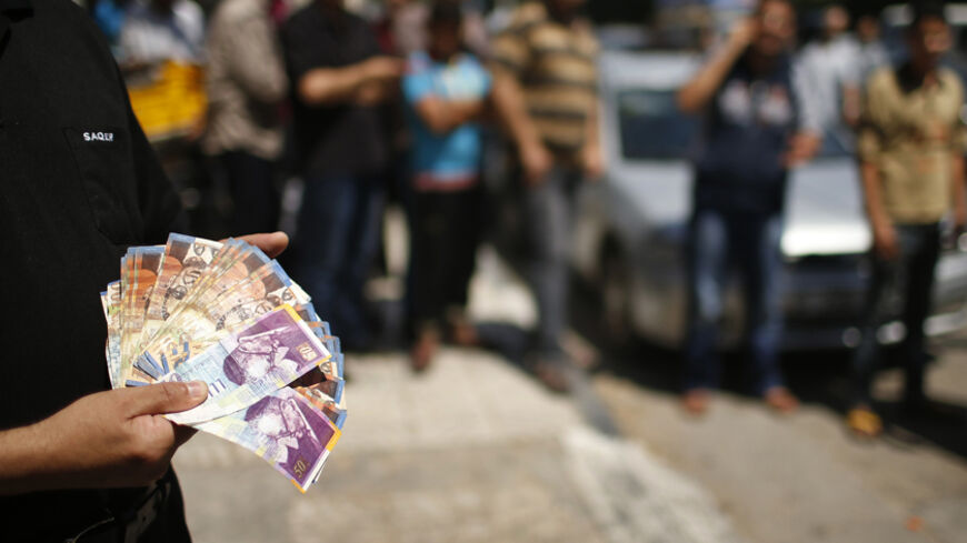 A Palestinian employee paid by the Palestinian Authority shows money to the camera after withdrawing cash from an ATM machine outside a bank, in Gaza City June 11, 2014. Gaza's public sector union suspended protests on Wednesday that had paralysed the local economy and threatened the deal on a Palestinian unity government but said it would resume its action if its members were not promptly paid. The pay dispute involving some 40,000 public servants erupted last week shortly after Hamas, which has ruled Gaza