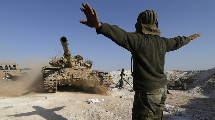 A Free Syrian Army (FSA) fighter gestures towards fellow fighters operating a tank during what the FSA said was an offensive to take control of al-Zaalana checkpoint in Wadi al-Deif military camp, which remains under government control, in the southern Idlib countryside July 9, 2014. Free Syrian Army fighters started the al-Jaysh al-Wahad (The One Army) battle against forces loyal to Syria's President Bashar al-Assad over the al-Hamidiyeh and Wadi al-Deif military camps in Idlib, trying to take control of t