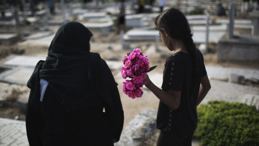 A Palestinian woman and a girl carry flowers to a family grave on Eid al-Fitr at a cemetery in Gaza City July 28, 2014. The U.N. Security Council agreed on a statement on Sunday urging Israel, Palestinians and Islamist Hamas militants to implement a humanitarian truce beyond the Muslim holiday of Eid al-Fitr, a festival marking the end of the Muslim holy fasting month of Ramadan, and engage in efforts to achieve a durable ceasefire REUTERS/Finbarr O'Reilly (GAZA - Tags: POLITICS MILITARY CIVIL UNREST RELIGI