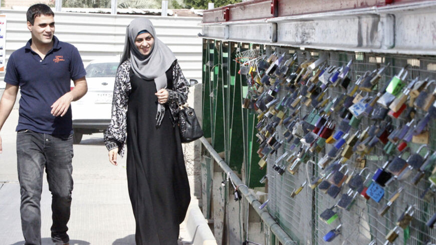 A couple walks on a bridge covered with padlocks hung by lovers in Basra, October 21, 2014. The idea was inspired by snapshots of Paris' Pont des Arts taken by a young Basra man on a visit to France, and was immediately embraced by the group of friends. Within a week, the men had received permission and turned one of the cities' old bridges which crosses over the Shatt-al-Arab waterway into Basra's own "Bridge of Love". REUTERS/ Essam Al-Sudani (IRAQ - Tags: SOCIETY) - RTR4B10I