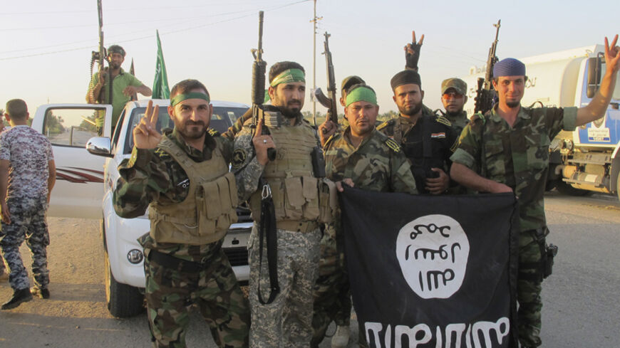 Shi'ite fighters pose with a black flag belonging to the Islamic State, which they pulled down after capturing the town of Jurf al-Sakhar from the Islamic State militants, south of Baghdad October 26, 2014. Picture taken October 26, 2014. REUTERS/Stringer (IRAQ - Tags: MILITARY POLITICS CIVIL UNREST CONFLICT) - RTR4BQ6H