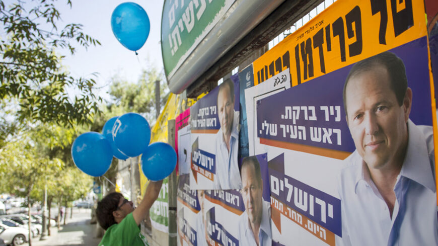 A supporter of the left wing Meretz party campaigning for municipal elections hangs balloons next to campaign posters of Jerusalem Mayor Nir Barkat in Jerusalem October 22, 2013. REUTERS/Baz Ratner (JERUSALEM - Tags: POLITICS ELECTIONS) - RTX14JPY