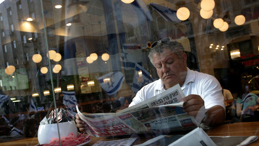 Israelis waving national flags are reflected in a coffee shop window as a man reads the newspaper during the annual Jerusalem Day parade in Jerusalem May 25, 2006. Jerusalem Day marks Israel's annual celebration of its capture of all of Arab East Jerusalem 39 years ago. REUTERS/Yonathan Weitzman - RTR1DREF