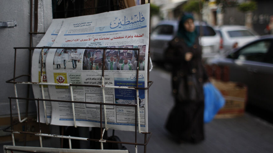 A Palestinian woman walks past copies of a pro-Hamas newspaper, Palestine, displayed outside a shop in the West Bank city of Ramallah May 10, 2014. The Palestinian authority had allowed the distribution of the pro-Hamas Palestine newspaper in the West Bank on Saturday after the Hamas-run government in the Gaza Strip said on Wednesday it had relaxed a ban on Palestinian newspapers published outside the enclave as a gesture of reconciliation to rival group Fatah after their unity deal last month. REUTERS/Moha