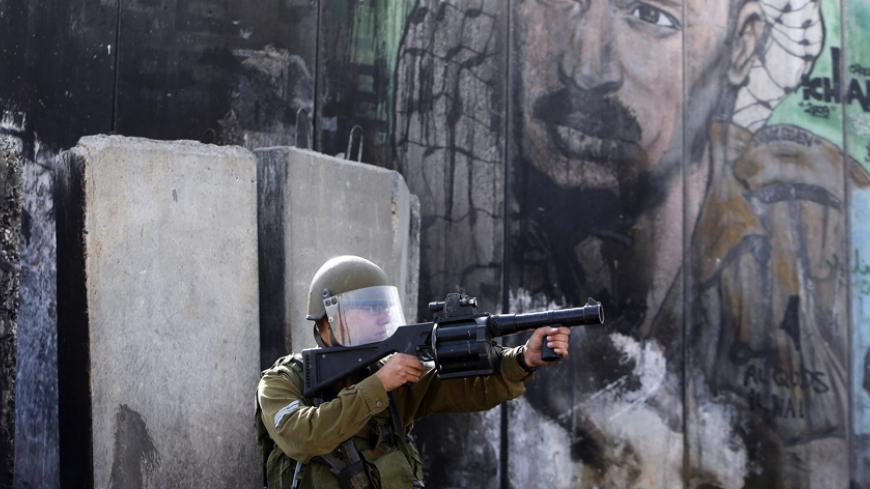 An Israeli solider points his weapon toward Palestinian protesters during clashes following an anti-Israel demonstration over the recent entry restrictions to the al-Aqsa mosque, at Qalandia checkpoint near the West Bank city of Ramallah November 2, 2014. A far-right politician who wants Jews to be allowed to pray at Jerusalem's al-Aqsa compound visited the site on Sunday, defying Prime Minister Benjamin Netanyahu's calls for restraint after clashes this week between Israeli police and Palestinians. Sunday 
