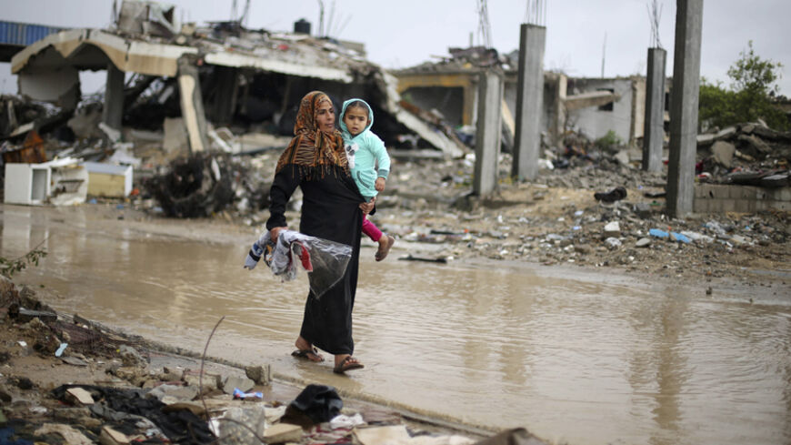 A Palestinian woman carries her daughter as she walks past her house, which witnesses said was destroyed by Israeli shelling during the most recent conflict between Israel and Hamas, following heavy rain in the east of Khan Younis in the southern Gaza Strip November 4, 2014. REUTERS/Ibraheem Abu Mustafa (GAZA - Tags: POLITICS CONFLICT ENVIRONMENT) - RTR4CQQ0