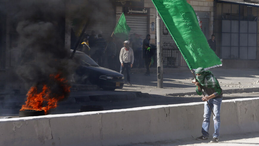 A Palestinian protester holds a Hamas flag during clashes with Israeli troops following a protest against what organizers say are recent visits by Jewish activists to al-Aqsa mosque, at Qalandia checkpoint near the West Bank city of Ramallah November 7, 2014. In recent months, a campaign for the prayer ban on Jewish worshippers at the site, known to Muslims as the Noble Sanctuary and to Jews as Temple Mount, to be overturned, led by settler activists, has gathered momentum, raising alarm among Palestinians 