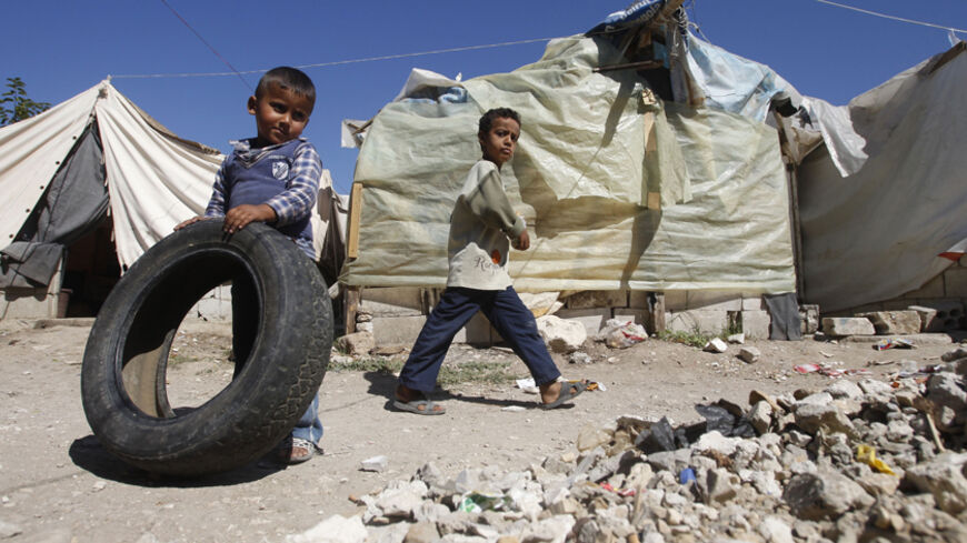 A Palestinian refugee boy from Syria plays with a tyre as another boy walks past tents at Ain al-Helweh Palestinian refugee camp near the port-city of Sidon, southern Lebanon October 8, 2013. International donors must do more to help Lebanon absorb a flood of refugees straining its schools and public services, the head of the United Nations children's fund UNICEF said. Picture taken October 8, 2013. REUTERS/Ali Hashisho (LEBANON - Tags: POLITICS CIVIL UNREST) - RTX14YGG