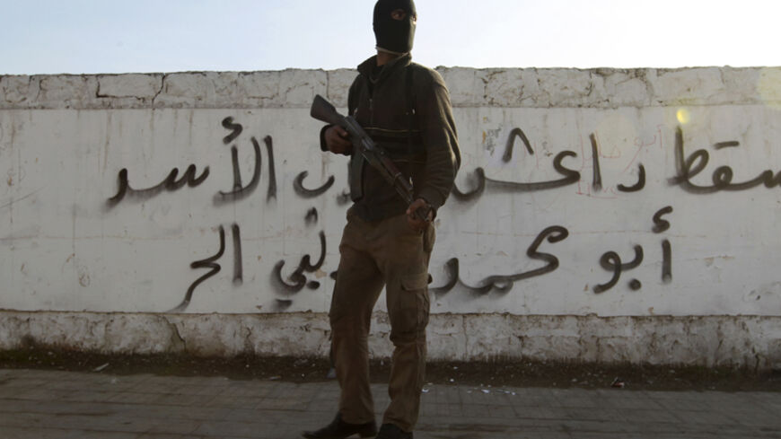 A Free Syrian Army fighter carries his weapon as he stands in front of graffiti that reads  "Daesh (Islamic State of Iraq and the Levant ) down" at Masaken Hanano neighborhood in Aleppo January 7, 2014. Five days of heavy rebel infighting has shaken the ISIL, which lost its main base in the northern city of Aleppo to rival rebels on Wednesday, according to a monitoring group. Picture taken January 7, 2014. REUTERS/Jalal Alhalabi (SYRIA - Tags: POLITICS CIVIL UNREST CONFLICT MILITARY) - RTX1767F