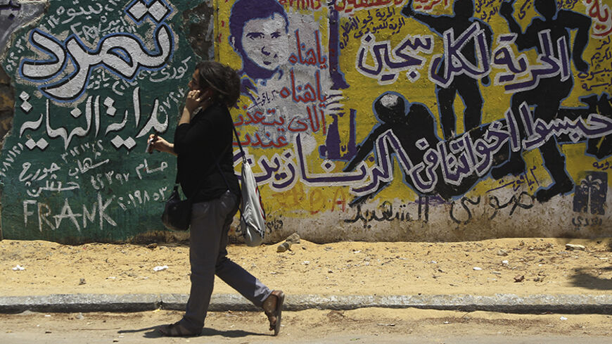 A woman walks past graffiti depicting riot police near Tahrir Square in Cairo June 23, 2013. The "Rebel!" alliance is campaigning to force President Mohamed Mursi to resign. Mursi's opponents say they have gathered about 15 million signatures - more than the 13 million votes that elected Mursi a year ago - on a petition calling on him to step down. The Arabic text reads, "Freedom for all prisoners locked our brothers in prison" (R) and "Tamarod (meaning 'Rebel!" alliance'), beginning of the end". REUTERS/Am