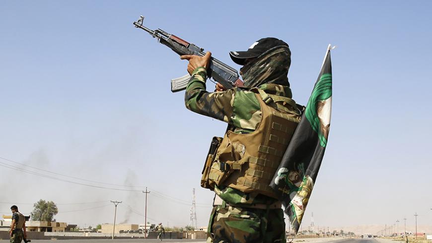 A fighter from the Shi'ite Badr Brigade militia wears a religious flag as he fires towards the air at a checkpoint recently taken from militants of the Islamic State outside the town of Amerli September 5, 2014. The highway, which continues south to Baghdad, is now controlled by Shi'ite militia fighters and the Kurdish Peshmerga. REUTERS/Ahmed Jadallah (IRAQ - Tags: CIVIL UNREST POLITICS CONFLICT) - RTR45475