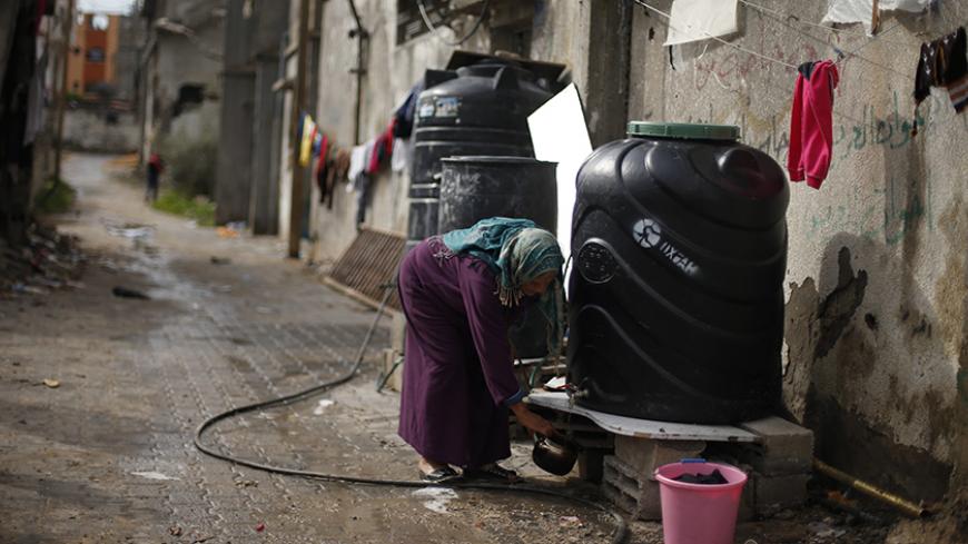 A Palestinian woman fills a kettle with water from a tank placed outside her house, that witnesses said was damaged by Israeli shelling during the July-August war between Israel and Hamas-led Gaza militants, in the east of Gaza City January 4, 2015. REUTERS/Suhaib Salem (GAZA - Tags: POLITICS CIVIL UNREST) - RTR4K04H