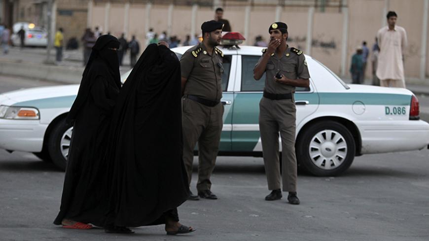 Women walk past members of Saudi security forces as they keep guard in Manfouha, southern Riyadh, November 14, 2013. A Sudanese man was killed in a second flare of clashes since Saturday between Saudi riot police, citizens and foreign workers in Riyadh amid a clampdown on visas, state media said late on Wednesday. The report on the official Saudi Press Agency, which cited a Riyadh police spokesman, gave no further details about the dead man, but said the clashes had started as a dispute between Saudis and f