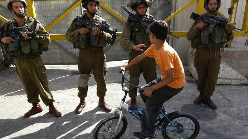 A Palestinian boy rides his bicycle past Israeli soldiers during a protest, by both Palestinian and foreign activists against the continued closure of Shuhada street to Palestinians, in the West Bank city of Hebron August 7, 2010. REUTERS/Ammar Awad (WEST BANK - Tags: CIVIL UNREST MILITARY IMAGES OF THE DAY) - RTR2H4DA