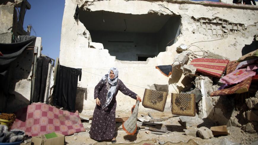 A Palestinian woman standing outside her damaged house watches a demonstration calling for Gaza reconstruction and against the United Nations decision to suspend payments for Palestinians, whose houses were damaged or destroyed during a 50-day war with Israel last summer, in Biet Hanoun in the northern Gaza Strip January 30, 2015. The main U.N. aid agency in the Gaza Strip said on Tuesday a lack of international funding had forced it to suspend payments to tens of thousands of Palestinians for repairs to ho