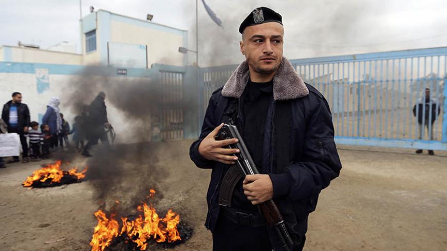 A Palestinian policeman loyal to Hamas stands guard near burning tyres during a protest by Palestinians calling for reconstruction of their houses that witnesses said were destroyed by Israeli shelling during a 50-day war last summer, outside a United Nations food distribution center in Rafah in the southern Gaza Strip February 16, 2015.  REUTERS/Ibraheem Abu Mustafa (GAZA - Tags: POLITICS CIVIL UNREST CRIME LAW) - RTR4PQSX