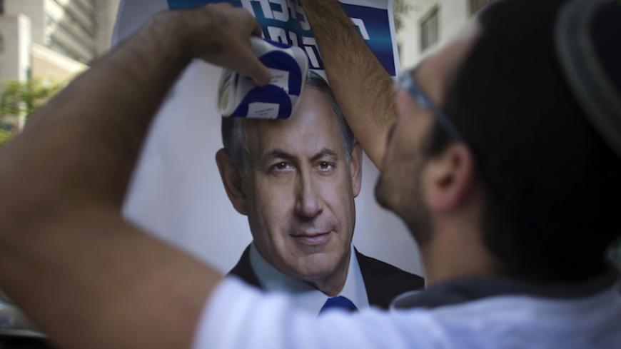 A Likud party supporter hangs a campaign poster depicting Prime Minister Benjamin Netanyahu in Jerusalem March 17, 2015. Millions of Israelis voted on Tuesday in a tightly fought election, with Netanyahu facing an uphill battle to defeat a strong campaign by the centre-left opposition to deny him a fourth term in office. REUTERS/Ronen Zvulun (JERUSALEM - Tags: POLITICS ELECTIONS) - RTR4TP77