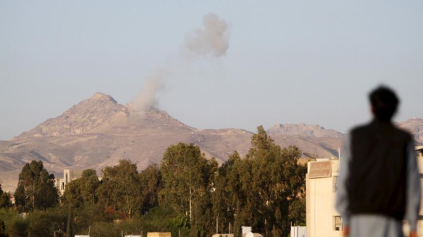 A man looks on as smoke billows from military barracks in the Jabal al-Jumaima mountain following an air strike near Sanaa March 30, 2015. REUTERS/Mohamed al-Sayaghi - RTR4VHP4