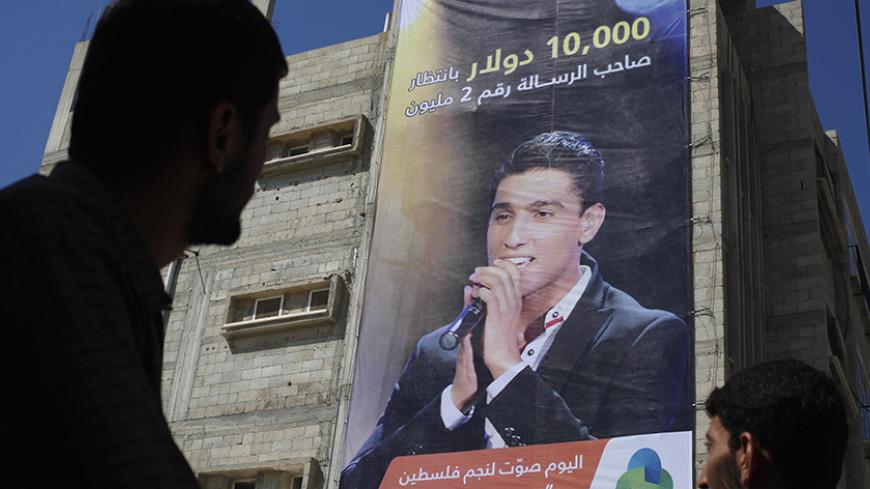 Palestinians look at a large poster depicting singer Mohammed Assaf in Khan Younis, in the southern Gaza Strip, June 20, 2013. Palestinian fans and big business are rallying behind Assaf, a 22-year-old singer from the Gaza Strip, in a final push to vote him the next "Arab Idol" in a TV talent contest choosing a winner in Beirut on Saturday. The Arabic words in the bottom of the poster read: "Vote for the star of Palestine Mohammed Assaf today". REUTERS/Ibraheem Abu Mustafa (GAZA - Tags: SOCIETY ENTERTAINMEN