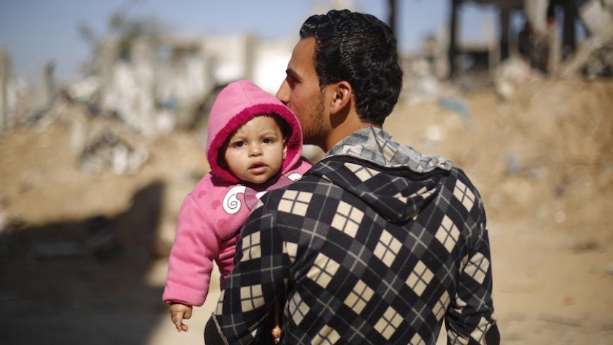 A Palestinian man carries his child on February 26, 2015 in Gaza City's al-Shejaiya neighbourhood next to buildings destroyed during the 50-day war between Israel and Hamas militants in the summer of 2014. More than 100,000 homes in the Gaza Strip were damaged or destroyed in Israeli bombardment during the 50-day conflict.  AFP PHOTO / MOHAMMED ABED        (Photo credit should read MOHAMMED ABED/AFP/Getty Images)