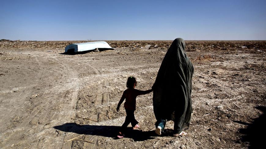 An Iranian woman walks with her daughter past an abandoned boat in Sikh Sar village at Hamoon wetland near the Zabol town, in southeastern province of Sistan-Baluchistan bordering Afghanistan on February 2, 2015. AFP PHOTO/BEHROUZ MEHRI        (Photo credit should read BEHROUZ MEHRI/AFP/Getty Images)